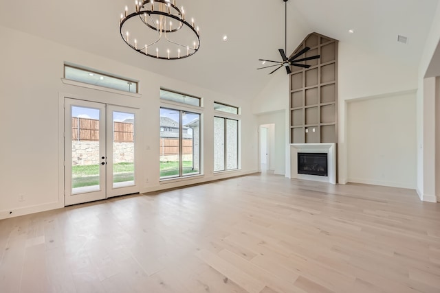 unfurnished living room with ceiling fan with notable chandelier, a fireplace, light wood-type flooring, and high vaulted ceiling