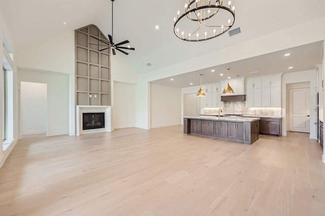 unfurnished living room featuring high vaulted ceiling, ceiling fan with notable chandelier, sink, a fireplace, and light hardwood / wood-style floors