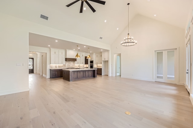 unfurnished living room featuring sink, light hardwood / wood-style floors, ceiling fan with notable chandelier, and high vaulted ceiling