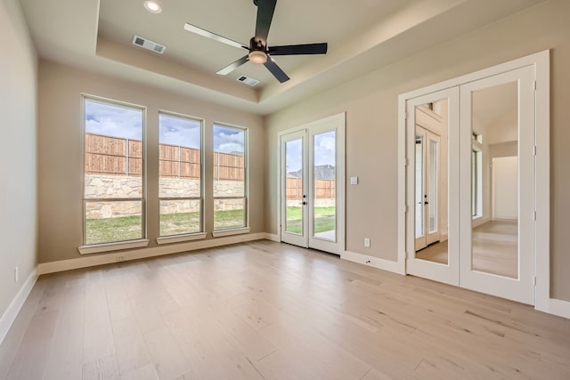 unfurnished room featuring french doors, ceiling fan, a raised ceiling, and light wood-type flooring