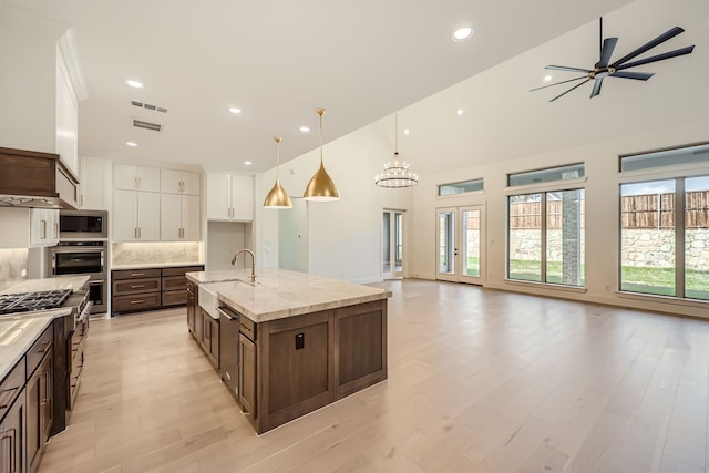 kitchen with hanging light fixtures, stainless steel appliances, a large island, sink, and white cabinets