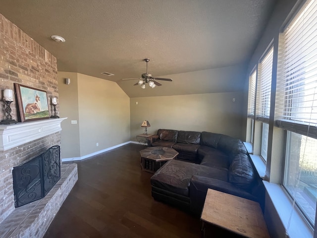 living room with lofted ceiling, dark wood-type flooring, a brick fireplace, ceiling fan, and a textured ceiling