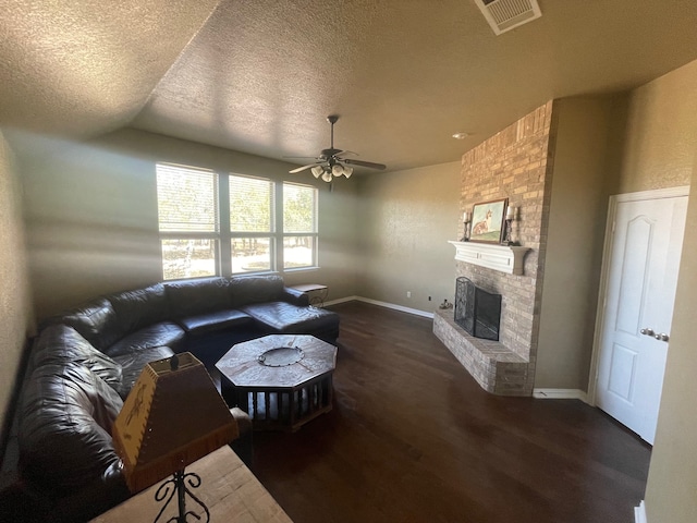 living room with ceiling fan, dark wood-type flooring, a brick fireplace, lofted ceiling, and a textured ceiling