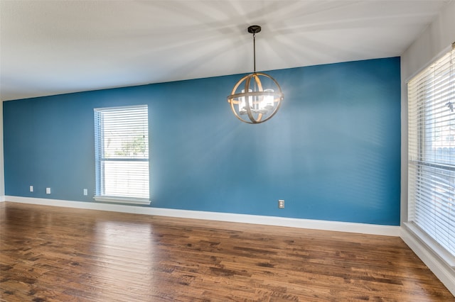 unfurnished room featuring a notable chandelier, dark wood-type flooring, and a wealth of natural light