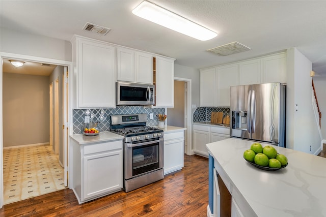 kitchen featuring light stone counters, tasteful backsplash, dark wood-type flooring, white cabinetry, and appliances with stainless steel finishes