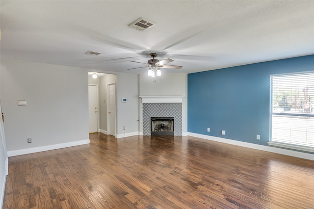 unfurnished living room with ceiling fan, a textured ceiling, hardwood / wood-style floors, and a tile fireplace