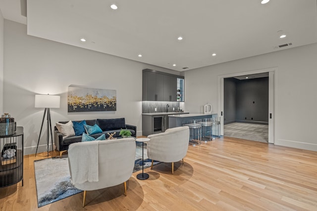 living room featuring beverage cooler, light wood-type flooring, and wet bar