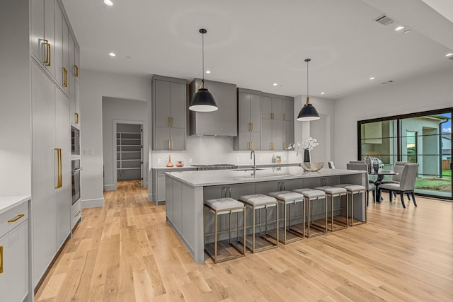 kitchen featuring an island with sink, gray cabinetry, stainless steel appliances, a kitchen bar, and pendant lighting