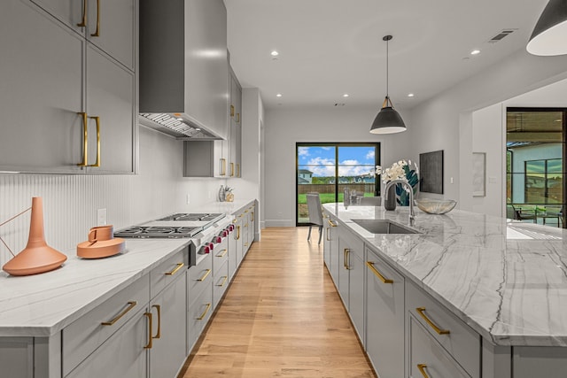 kitchen featuring a large island, wall chimney range hood, gray cabinetry, and decorative light fixtures