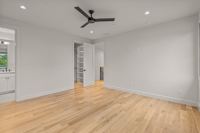unfurnished bedroom featuring a walk in closet, light wood finished floors, baseboards, and ensuite bathroom