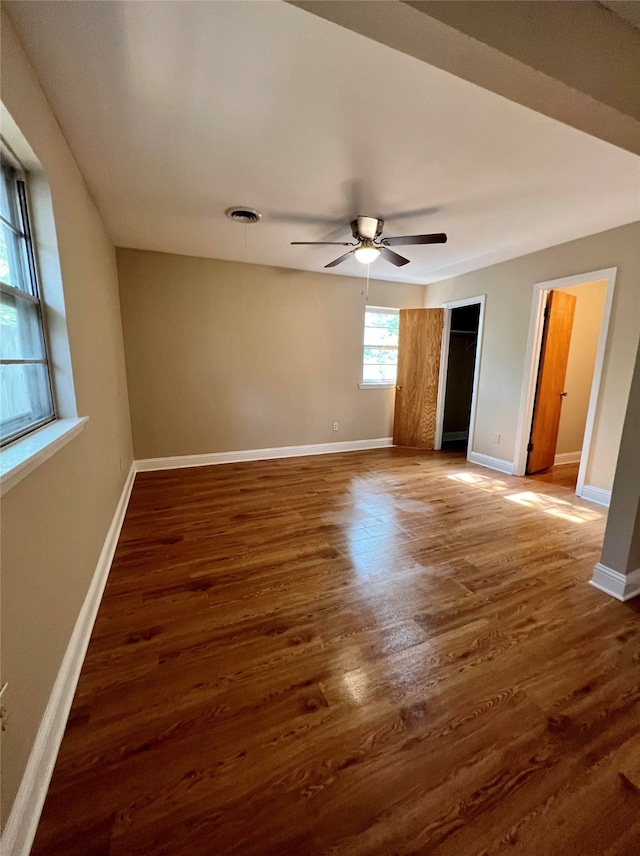 unfurnished bedroom with a spacious closet, ceiling fan, and dark wood-type flooring