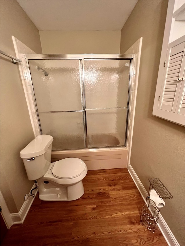 bathroom with combined bath / shower with glass door, hardwood / wood-style floors, and toilet