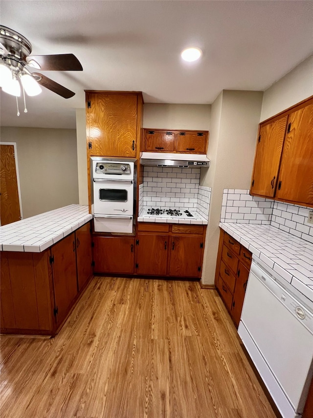 kitchen featuring light hardwood / wood-style floors, kitchen peninsula, decorative backsplash, white appliances, and ceiling fan