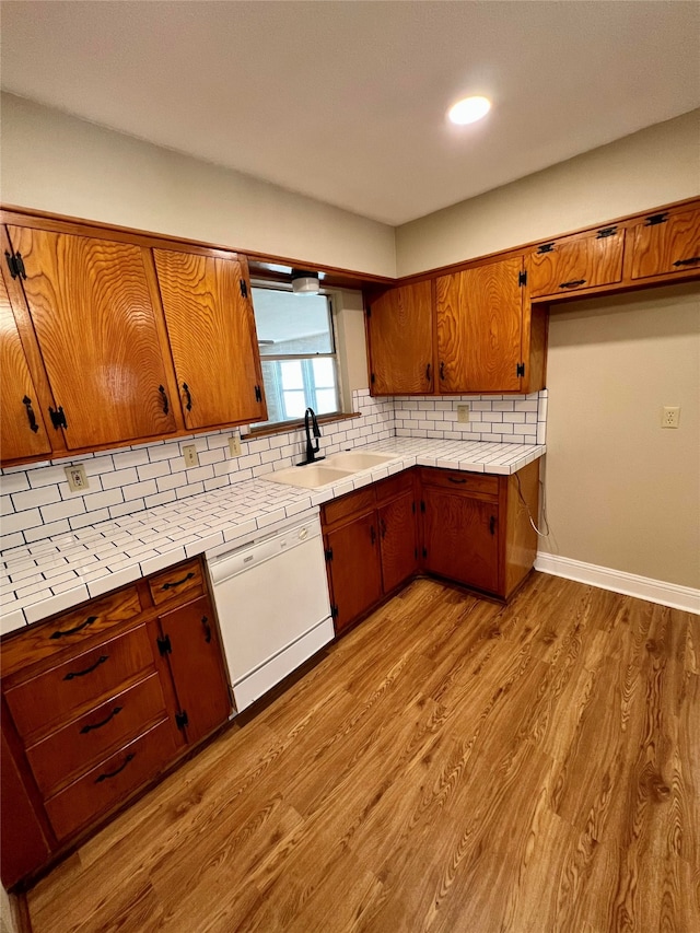 kitchen with light wood-type flooring, backsplash, white dishwasher, and tile countertops