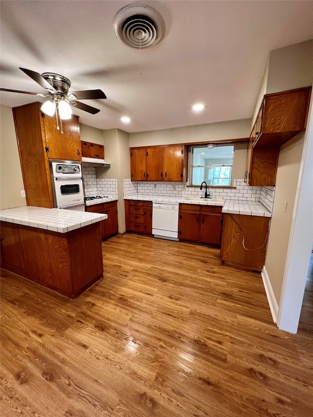 kitchen featuring ceiling fan, kitchen peninsula, white appliances, tile counters, and light wood-type flooring