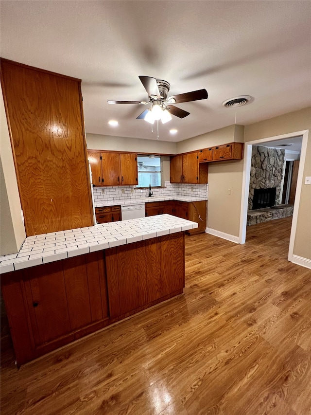 kitchen with kitchen peninsula, white dishwasher, tile countertops, ceiling fan, and hardwood / wood-style flooring