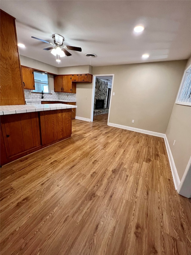 kitchen featuring hanging light fixtures, light hardwood / wood-style floors, kitchen peninsula, tile countertops, and ceiling fan