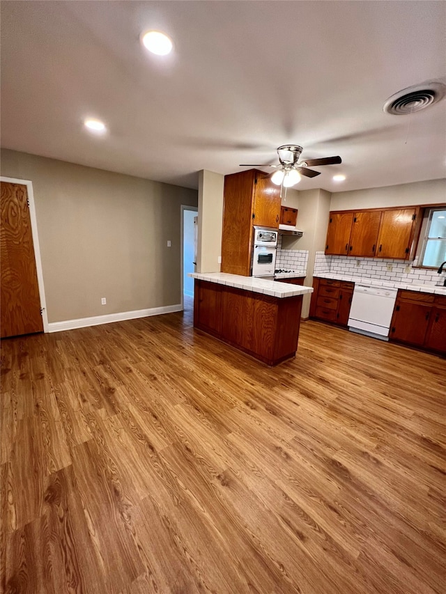 kitchen featuring ceiling fan, kitchen peninsula, white appliances, light hardwood / wood-style flooring, and decorative backsplash