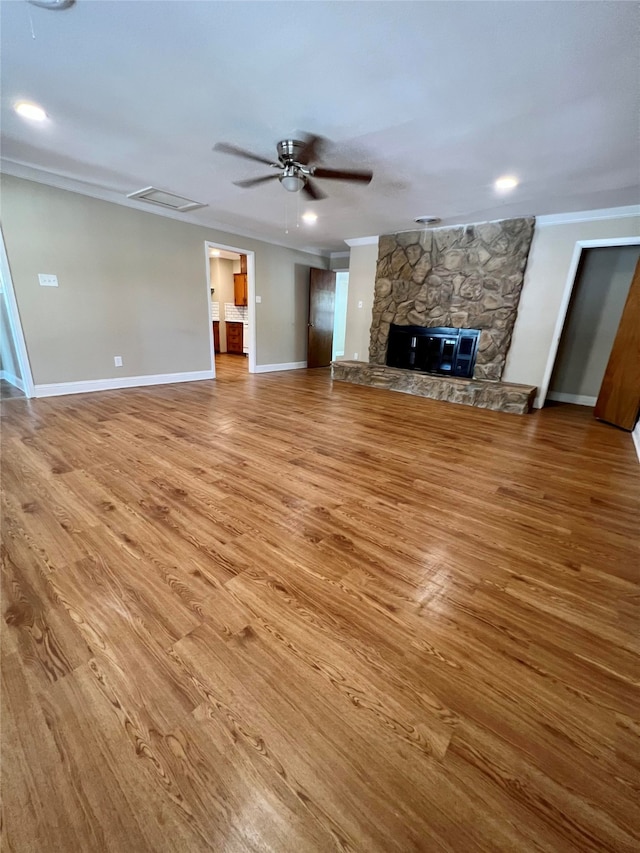 unfurnished living room with ceiling fan, a stone fireplace, light wood-type flooring, and crown molding