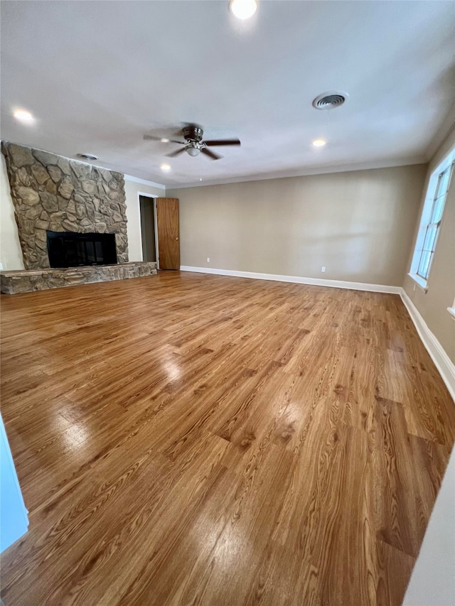 unfurnished living room with ceiling fan, a stone fireplace, and hardwood / wood-style floors