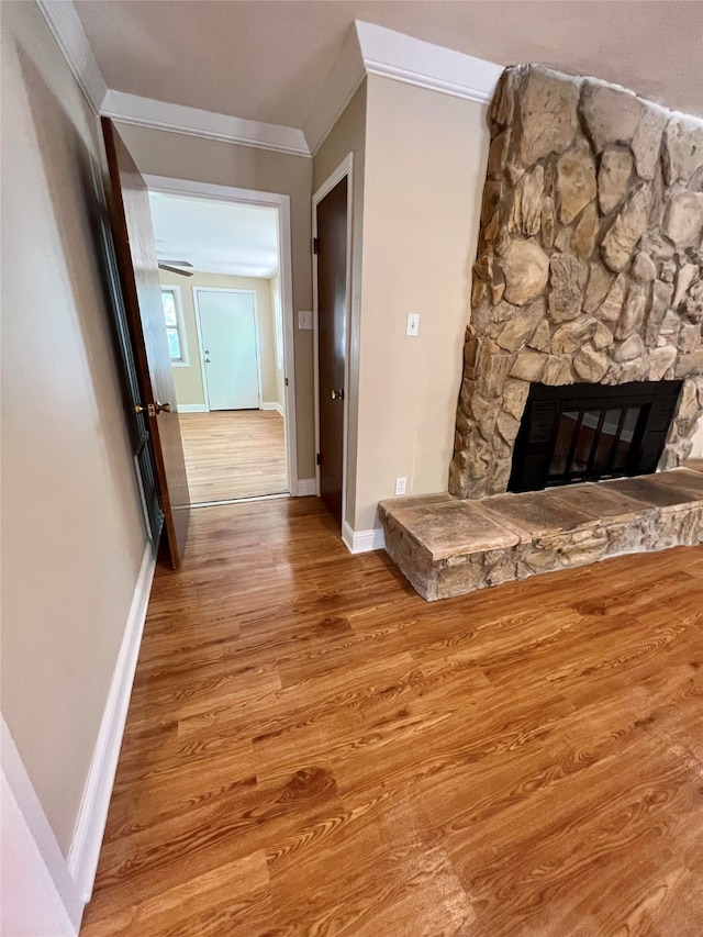 unfurnished living room featuring a stone fireplace, light hardwood / wood-style flooring, and ornamental molding