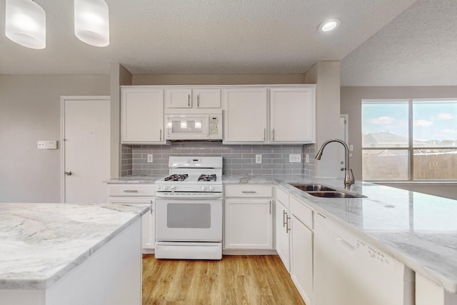 kitchen with white appliances, backsplash, white cabinets, sink, and hanging light fixtures