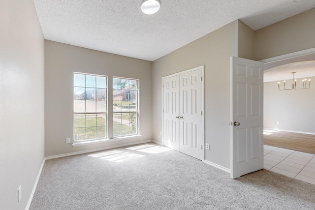 unfurnished bedroom with light carpet, a textured ceiling, an inviting chandelier, and a closet