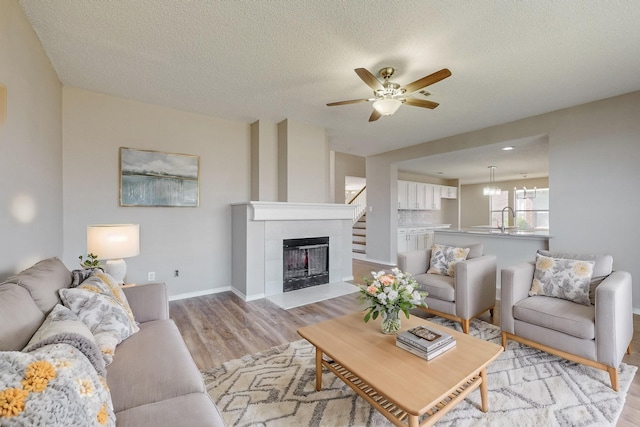 living room with a tile fireplace, ceiling fan, sink, light hardwood / wood-style flooring, and a textured ceiling