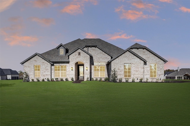 french provincial home featuring a front yard, brick siding, and roof with shingles