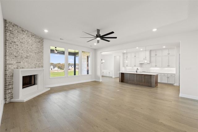 unfurnished living room featuring a fireplace, light wood-type flooring, ceiling fan, and sink