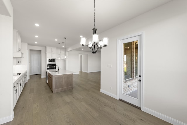 kitchen featuring a center island with sink, oven, light countertops, white cabinetry, and pendant lighting