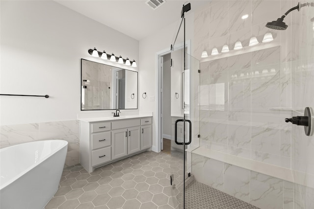 full bathroom with visible vents, a freestanding bath, vanity, a shower stall, and tile walls