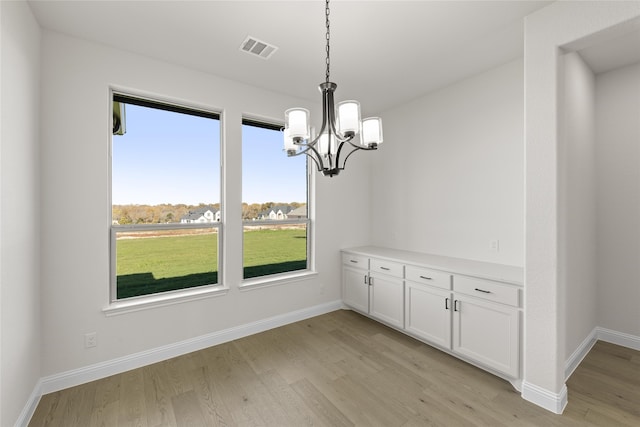 unfurnished dining area featuring a healthy amount of sunlight, light hardwood / wood-style floors, and a notable chandelier