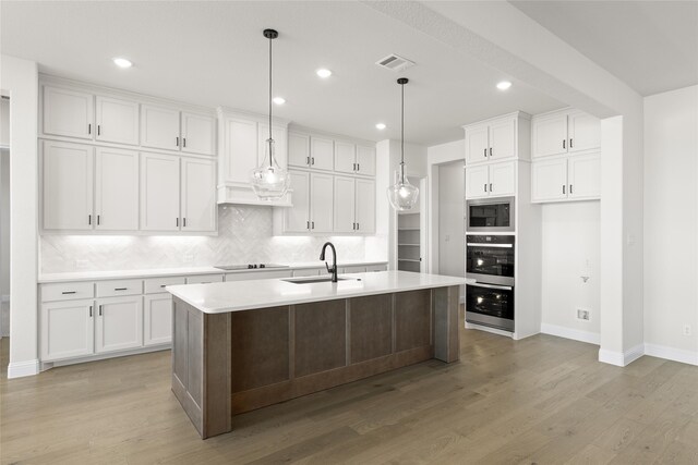 kitchen featuring white cabinets, pendant lighting, a center island with sink, and appliances with stainless steel finishes