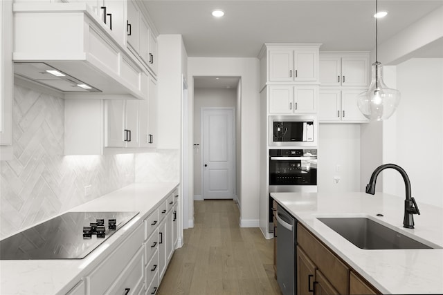 kitchen featuring pendant lighting, custom exhaust hood, appliances with stainless steel finishes, white cabinetry, and a sink