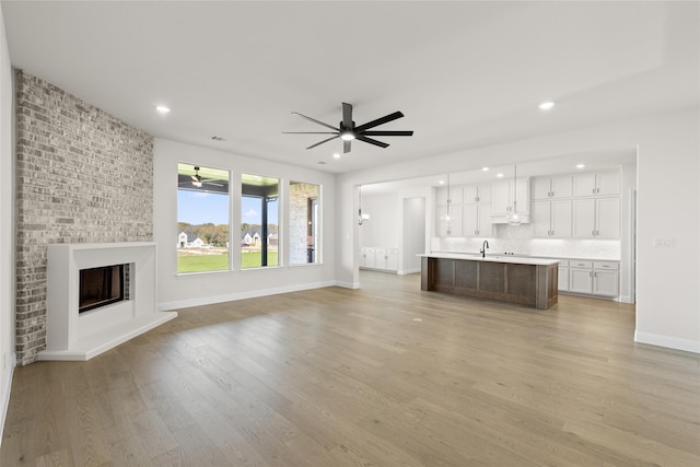 unfurnished living room featuring ceiling fan, recessed lighting, light wood-type flooring, and a brick fireplace