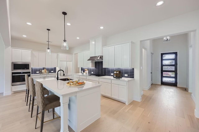 kitchen featuring white cabinets, a center island with sink, oven, and sink