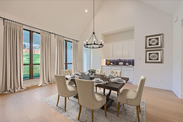 dining area with light wood-type flooring, high vaulted ceiling, and a chandelier