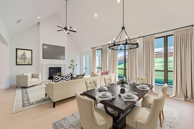 dining room with ceiling fan with notable chandelier, high vaulted ceiling, and light hardwood / wood-style flooring