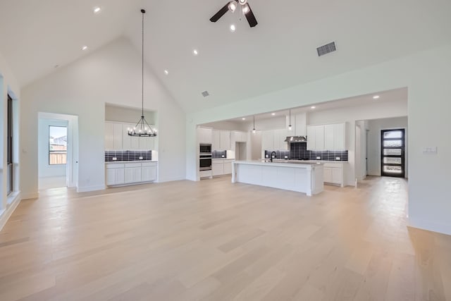 unfurnished living room with ceiling fan with notable chandelier, light hardwood / wood-style flooring, high vaulted ceiling, and sink