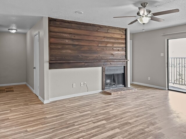 unfurnished living room with a brick fireplace, a textured ceiling, light hardwood / wood-style floors, and ceiling fan