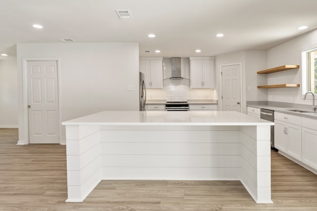 kitchen with wall chimney exhaust hood, white cabinetry, a center island, and light hardwood / wood-style flooring