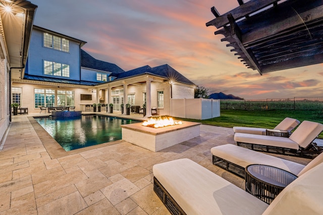 pool at dusk featuring a yard, an outdoor living space with a fire pit, and a patio area