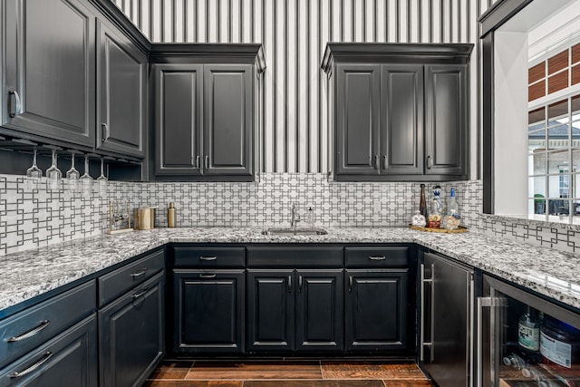 kitchen featuring refrigerator, sink, light stone counters, and beverage cooler