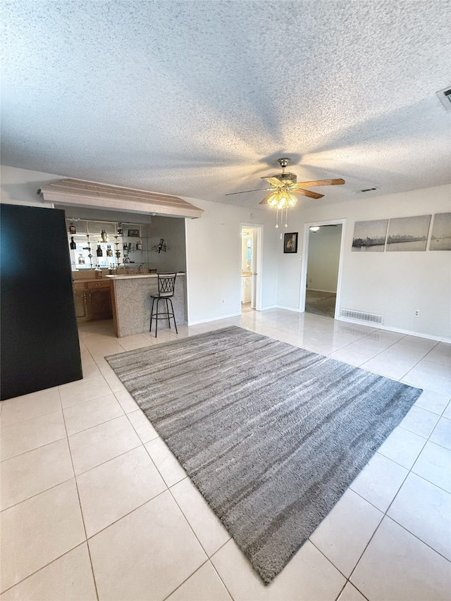 unfurnished living room with a textured ceiling, light tile patterned flooring, and ceiling fan