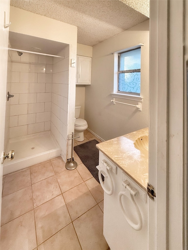 bathroom featuring vanity, tiled shower, a textured ceiling, tile patterned floors, and toilet