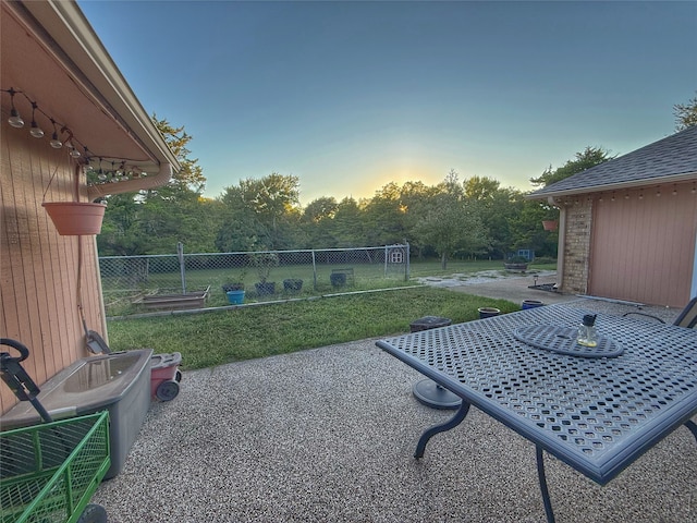 patio terrace at dusk featuring a lawn