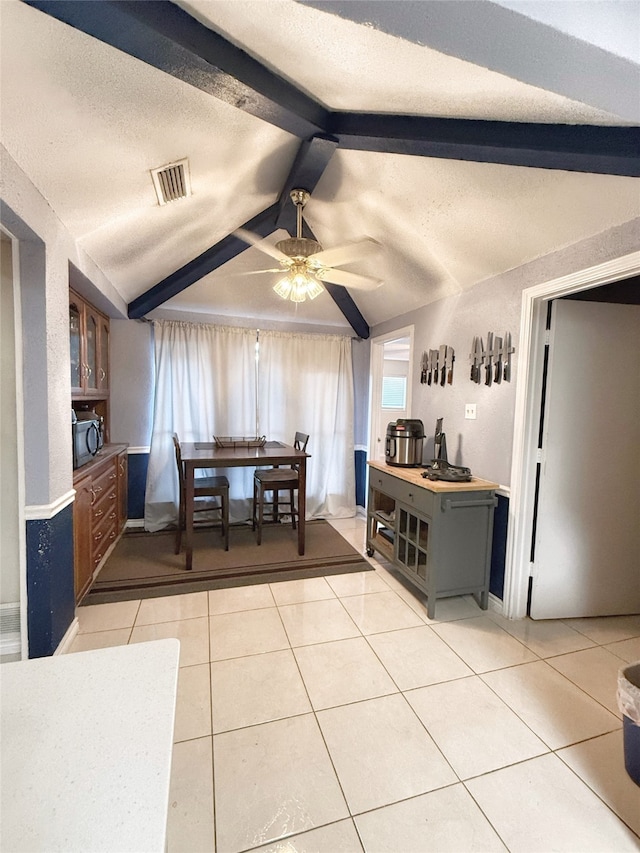 tiled dining area featuring vaulted ceiling with beams, ceiling fan, and a textured ceiling