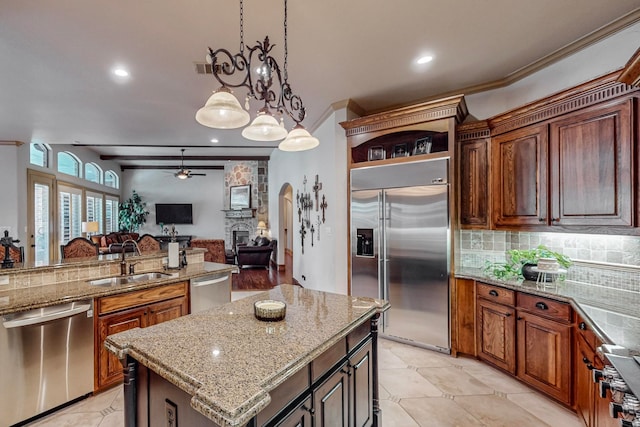 kitchen with sink, tasteful backsplash, a stone fireplace, stainless steel appliances, and a center island