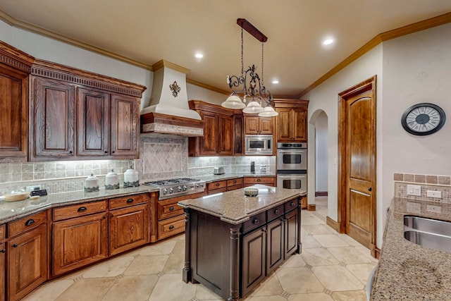 kitchen with custom range hood, light stone counters, backsplash, stainless steel appliances, and a center island